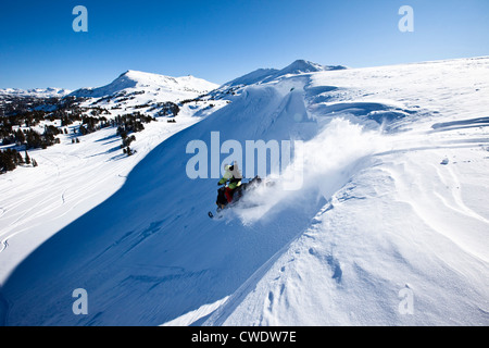 Ein Snowmobiler Sprung von einem Gesims an einem sonnigen Wintertag in Montana. Stockfoto