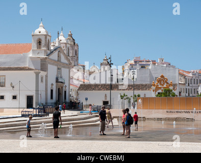 Kirche von Santa Maria in Lagos, Portugal mit Menschen spielen in den Wasserfontänen in den Vordergrund Praça Infante Dom Henri Stockfoto