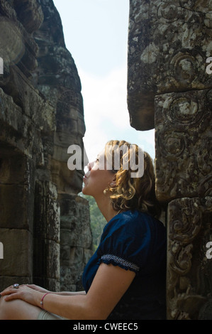 Vertikale Porträt eines westlichen Touristen, die vorgibt, eines der vielen geschnitzten Gesichter im Bayon Tempel in Siem Reap zu küssen. Stockfoto