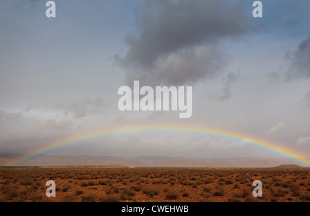 Voller Regenbogen über der Sahara in Afrika mit teilweise bewölktem Himmel und Atlas Gebirge im Hintergrund Stockfoto