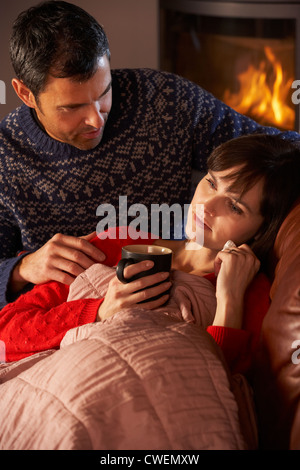 Mann Pflege kranke Frau mit kalten ruhen auf Sofa gemütliche Kaminfeuer Stockfoto