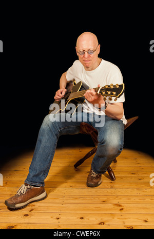 Mann, der eine e-Gitarre mit einem Plektrum vor einem schwarzen Hintergrund, Fokus auf der Gitarre spielt Stockfoto