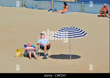 Ältere Sonnenanbeter schlafen im liegen neben Schatten Sonnenschirm und bekommen Sonnenbrand im Sommer entlang der Nordseeküste Stockfoto