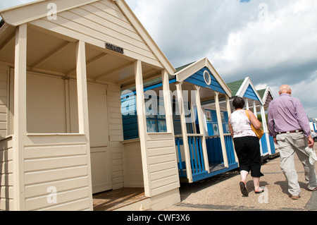 Älteres Ehepaar vorbeigehen trendige traditionelle und teure Holz Strandhütten am Strand von Suffolk Küstenstadt Southwold Stockfoto