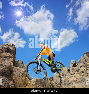 Person Reiten ein Mountain bike Mitte Felsen an einem sonnigen Tag gegen einen blauen Himmel und Wolken, niedrigen Winkel Ansicht Stockfoto