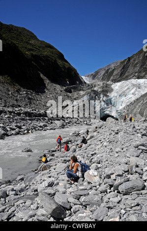 Besucher am Ufer eines schnell fließenden Flusses am Franz-Josef-Gletscher auf Südinsel in Neuseeland Stockfoto