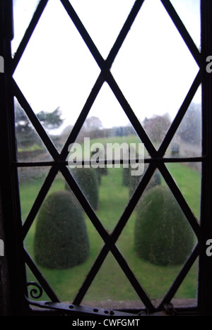 Blick durch ein Blei-paned Fenster heraus zum Formschnitt Büsche Stockfoto