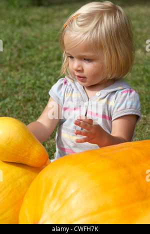 Cute blonde Kind Baby Mädchen ein Jahr alt sitzen und spielen mit Kürbissen Sommergarten Stockfoto