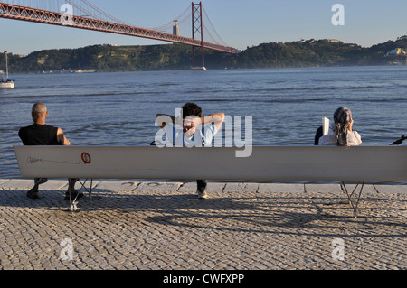 Leute sitzen auf Bank durch den Fluss Tejo in Lissabon, Portugal Stockfoto