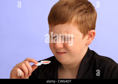 Ein 12 Jahre alter Junge zeigt seine Abneigung für die Medizin, die er nehmen soll Stockfoto