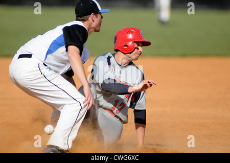 Baseball-Laufsohle gleitet sicher in Dritte mit der dritte Baseman versucht, einen Tag während einer High-School-Spiel zu machen. Stockfoto