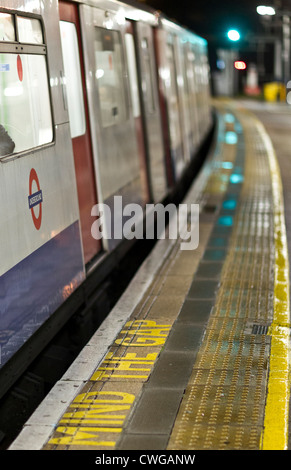 Eine Londoner u-Bahn am Bahnsteig in der Nacht, die Warnung "MIND THE GAP" in den Vordergrund, der Hintergrund unscharf. Stockfoto