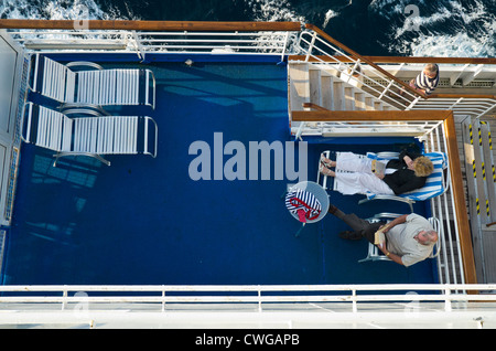 Zwei Passagiere sitzen auf dem Deck eines Kreuzfahrtschiffes zu lesen, während ein Drittel vorbei, geht von oben nach unten gesehen Stockfoto