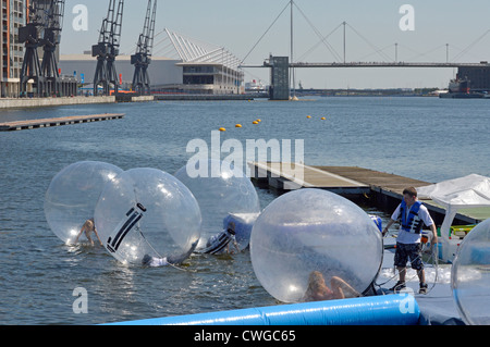 Kinder, die in gefesselten Zorbierbläschen im Aqua Balls Facility Minder spielen, der im Royal Docks Silvertown Newham London England UK teilnimmt Stockfoto