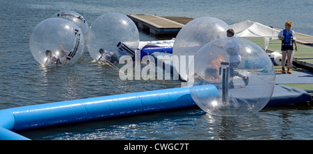 Kinder spielen in gefesselte aufblasbare Bläschen am dock Wasser bei Aqua Kugeln Anlage mit Aufpasser anwesend Stockfoto