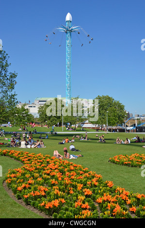Menschen entspannen unter den bunten Blumenbeeten in Jubilee Gardens mit Star Flyer Stuhl Fahrt über Stockfoto