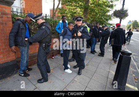 Metropolitan-Polizisten halten an und durchsuchen eine Gruppe schwarzer Jugendlicher am Notting Hill Carnival, London, England, Großbritannien. Stockfoto