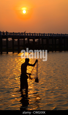 Ein Fischer wirft sein Netz unter U KLANGKUNST Brücke auf Taungthaman See bei Sonnenaufgang - AMARAPURA, MYANMAR Stockfoto