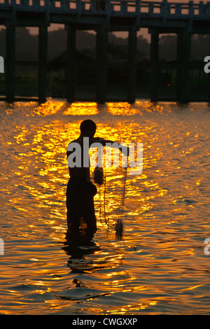 Ein Fischer wirft sein Netz unter U KLANGKUNST Brücke auf Taungthaman See bei Sonnenaufgang - AMARAPURA, MYANMAR Stockfoto