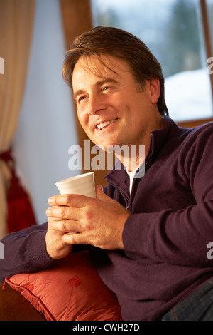 Applying Mann mit Heißgetränk auf Sofa vor dem Fernseher entspannen Stockfoto