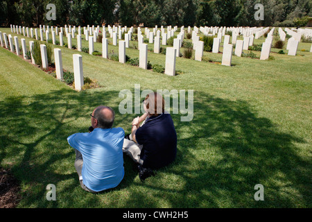 Besucher aus Großbritannien sitzen zwischen Gräbern auf dem Commonwealth war Graves Commission Cemetery und Memorial to the Vermissten für Personal der beiden Weltkriege und der Zeit des Mandats Palästina in der Stadt Ramla oder Ramle in Israel Stockfoto