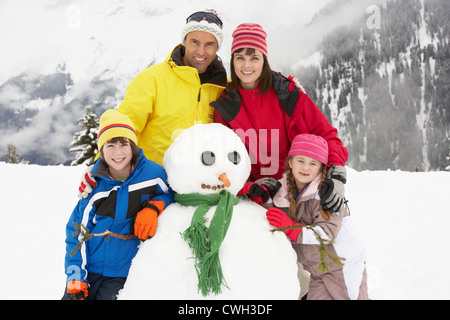 Familie Gebäude Schneemann auf Ski-Urlaub In Bergen Stockfoto