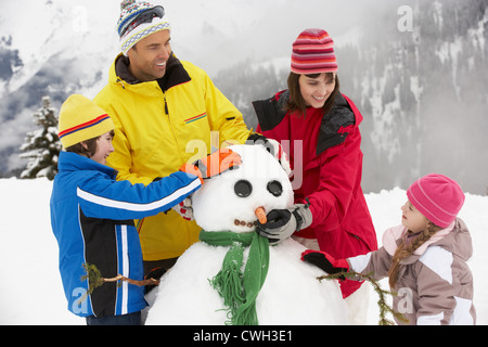 Familie Gebäude Schneemann auf Ski-Urlaub In Bergen Stockfoto