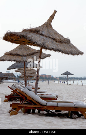 Sonnenliegen am Strand mit tropischen Sonnenschirmen Stockfoto