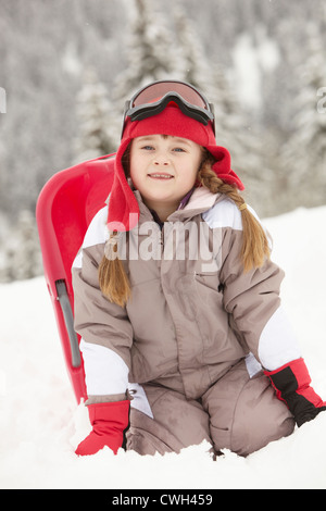 Junge Mädchen spielen im Schnee mit Schlitten auf Skiurlaub In Bergen Stockfoto