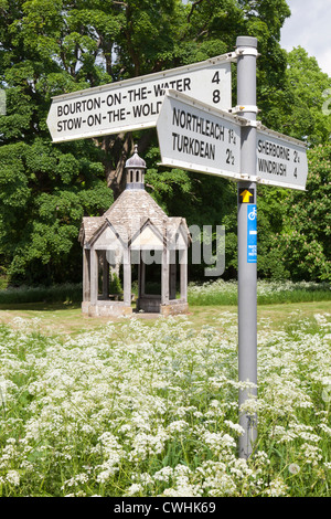 Wegweiser auf dem Dorfplatz & 1874 Pumphouse für die Wasserversorgung in die Cotswold Dorf Farmington, Gloucestershire Stockfoto