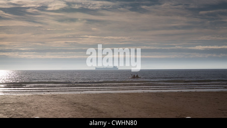 Kanuten in der Silhouette am Broadhaven Strand, Pembrokeshire, mit Schiff am Horizont für Milford Haven bestimmt. Stockfoto