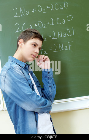 Nachdenkliche junge stehend von Blackboard und Formeln drauf an Stockfoto