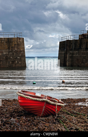 Ein kleine rote hölzernen Fischerboot vor Anker im Hafen von Mousehole Cornwall mit Gewitterwolken am Horizont. Stockfoto