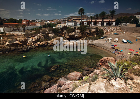 Badegäste und Sonnenanbeter genießen Sie die mediterrane Sonne in einer kleinen Bucht auf Isla Plana mit entfernten Palmen. In der Nähe von Mazarron Stockfoto