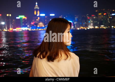 Eine Mädchen sitzt auf der Kowloon Seite der Victoria Bay Blick auf die Wolkenkratzer und Geschäft Bezirk von Hong Kong Island. Stockfoto