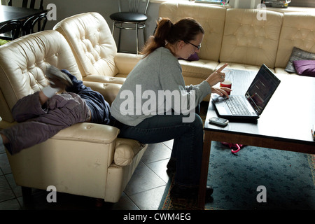 Polnische Frau, die versucht, auf ihrem Computer zu konzentrieren, während Sohn hinter ihr Alter 6 und 32, um tritt. Zawady Zentralpolen Stockfoto