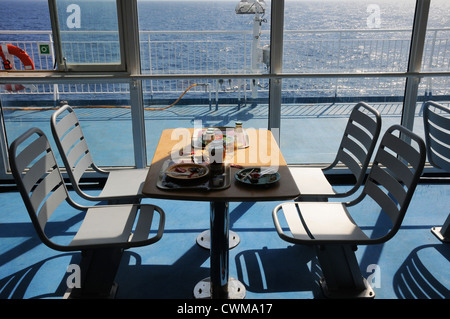 Frühstück, Essen, halbe gegessen, unvollendet, am Tisch mit vier Stühlen befestigt an Deck, hinter Fenster auf Deck mit Blick aufs Meer Stockfoto