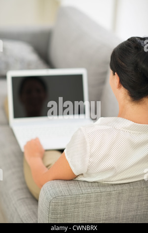 Junge Frau auf die Couch legen und am Laptop arbeiten. Ansicht von hinten Stockfoto