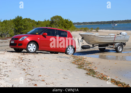 Roten Suzuki swift Unterstützung Bootsanhänger ins Wasser über den Strand Stockfoto