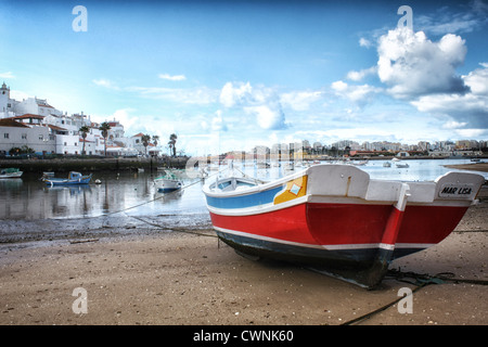 Farbige typisches Fischerboot auf nassen Sand bei Ebbe mit Ferragudo typische Fischerdorf in den Rücken und ein cloudysky Stockfoto