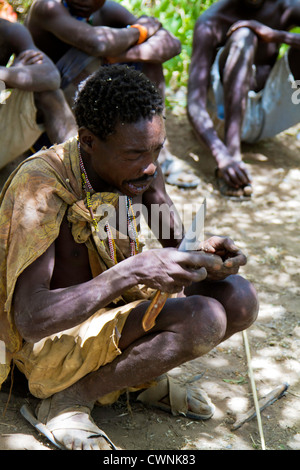 Hadza oder Hadzabe, eine ethnische Gruppe im Norden von Tansania, um Lake Eyasi Leben. Dieser Mann ist einen Speer für die Jagd Schnitzerei Stockfoto