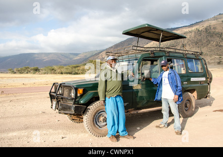 NGORONGORO KRATER, Tansania – Ein Safari-Guide und Koch posiert neben ihrem Toyota Landcruiser auf dem Boden des Ngorongoro Kraters im Ngorongoro Conservation Area, Teil des nördlichen Rundkreises von Nationalparks und Naturschutzgebieten Tansanias. Stockfoto