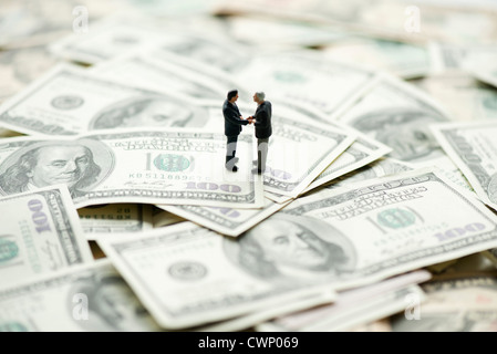 Männliche Figuren Händeschütteln auf Haufen von hundert-Dollar-Scheine Stockfoto