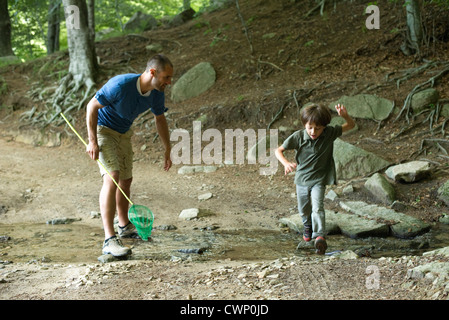 Vater und Sohn in Wäldern, junge, springen über stream Stockfoto