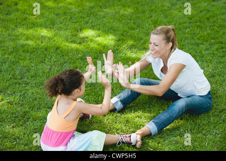 Mutter und Tochter sitzen auf dem Rasen spielen Patty-Kuchen Stockfoto