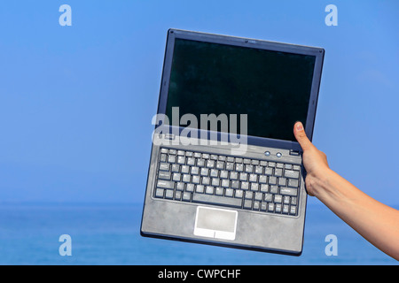 Hand hält einen Laptop auf dem Meer vor blauem Himmel Stockfoto