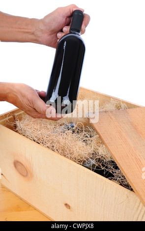 Mann hält eine einzelne Flasche Weine über hölzerne Kiste gefüllt mit Flaschen und Verpackungsmaterial. Vertikale isoliert auf weiß. Stockfoto