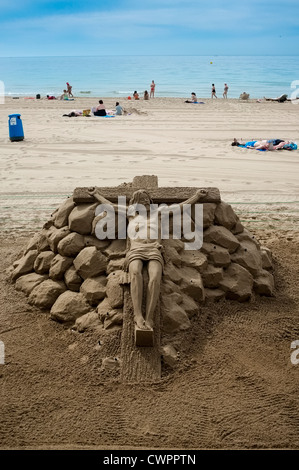 Eine Sandskulptur Jesu Christi am Kreuz auf dem Strand von Benidorm Levante. Stockfoto