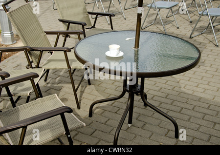 Leere Kaffeetasse auf Tisch und Stühlen auf Asphalt. Café im Freien. Stockfoto