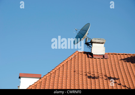 Satelliten-TV-Antenne angeschlossen an Schornstein auf rotem Ziegeldach Haus im Hintergrund des blauen Himmels. Stockfoto